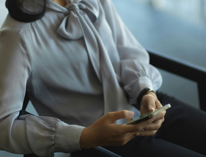 Person in a blouse holding a smartphone, reflecting on mental health challenges.