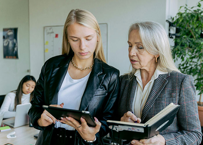 Two women in a workplace discussing over a tablet and a notebook, illustrating signs of a toxic workplace environment.