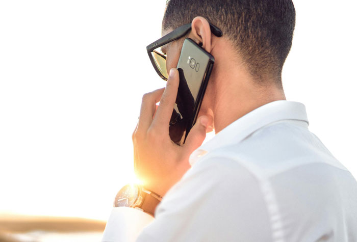 Man in glasses and white shirt talking on a mobile phone, with the sun setting in the background, focused on saving life tips.