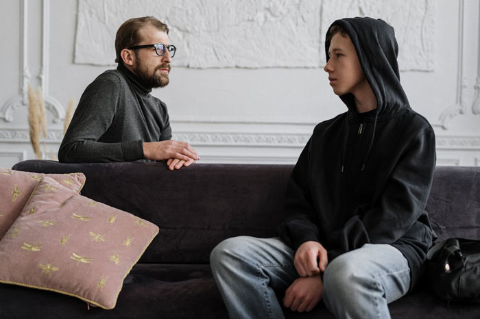 Man and teen talking on a couch, reflecting a parent-child interaction at home.