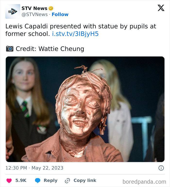 Statue with unique Scottish humor crafted by pupils, with a blurred background of students at an event.