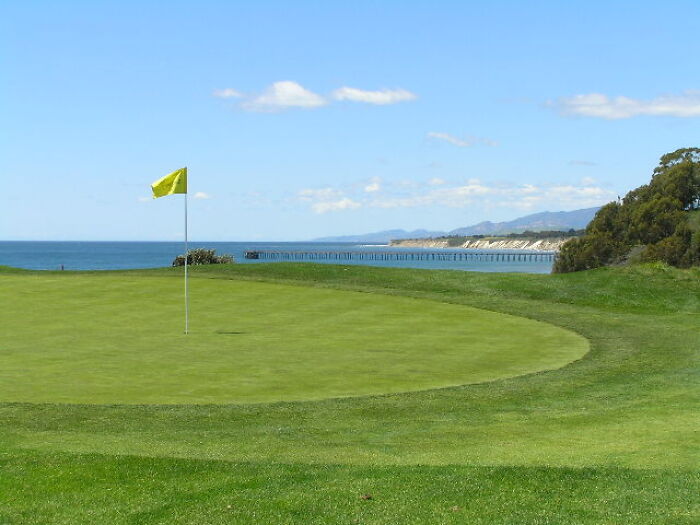 Golf course by the sea with a yellow flag, showcasing breathtaking scenery.