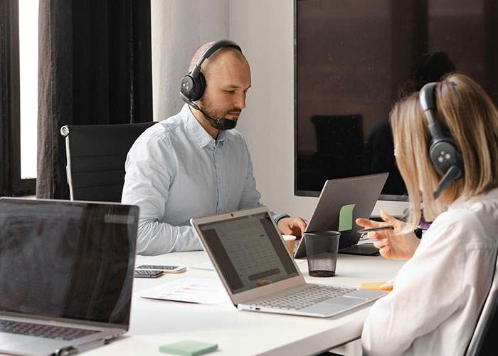 Two employees with headsets working at laptops, possibly indicating a toxic workplace environment.