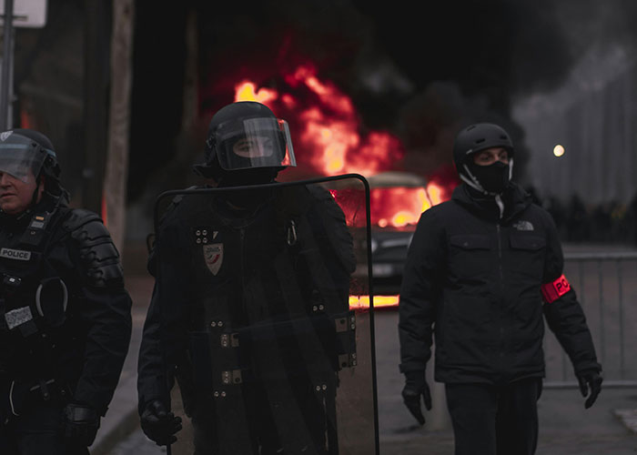 Police in riot gear near a fire, highlighting chaos in a scene reminiscent of life without social media.