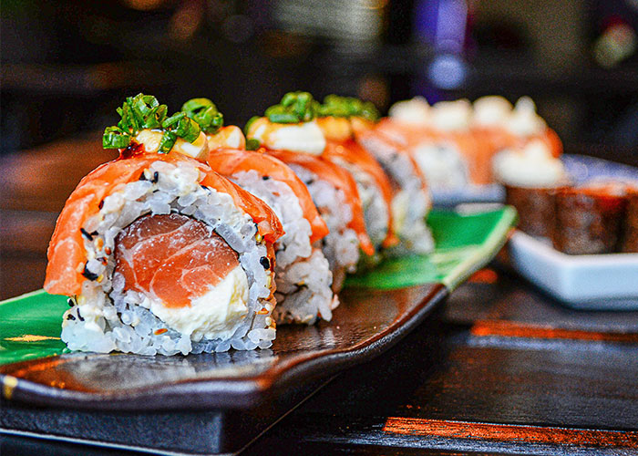 Sushi rolls on a black plate, featuring vibrant toppings, highlighting once exotic foods.