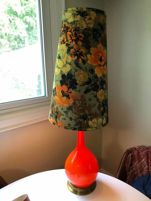 Unusual thrifted item: a lamp with a bright orange base and floral lampshade on a white table by a window.