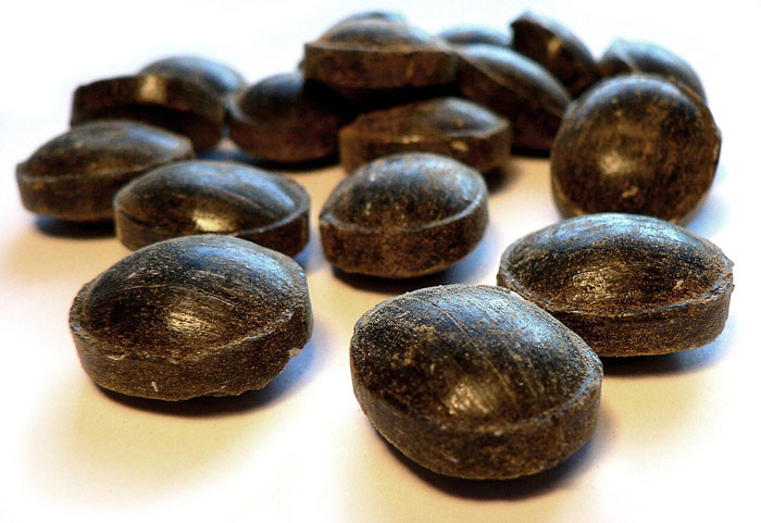 Old-school delicacies: Close-up of dark candy lozenges on a white surface.