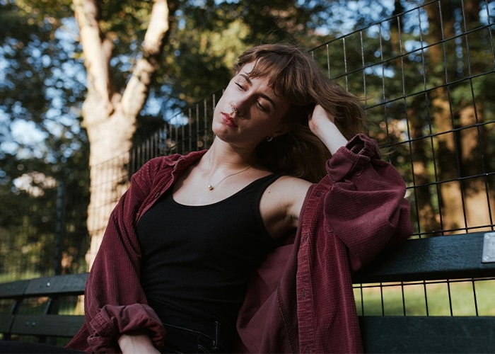Woman resting on a park bench, wearing a maroon shirt and black top, reflecting on parenting mistakes in natural light.