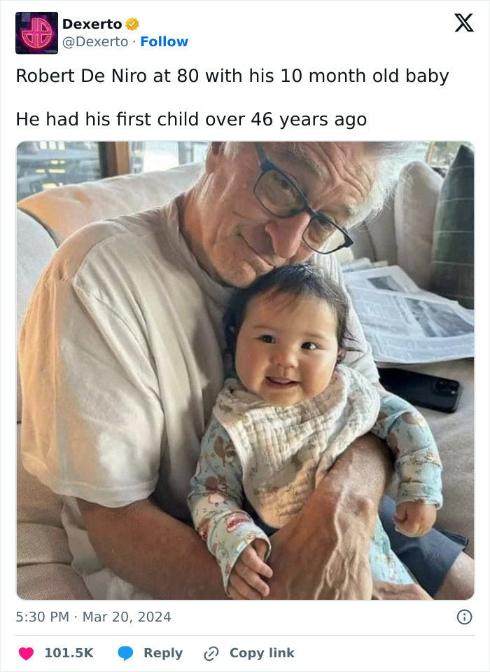 Robert De Niro, aged 80, smiling while holding his 10-month-old baby in his arms on a sofa. Robert De Niro, aged 80, smiling while holding his 10-month-old baby in his arms on a sofa.