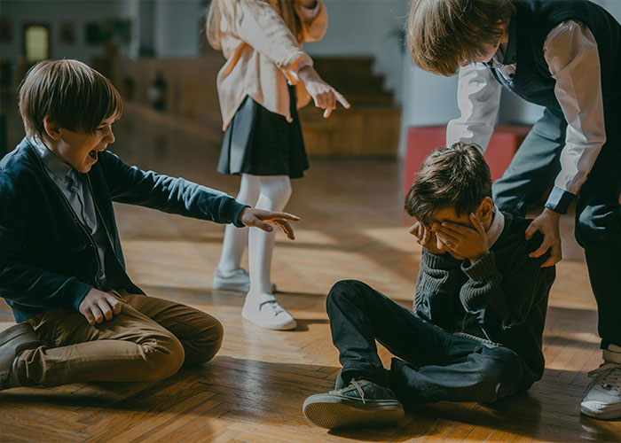 A child sits on the floor, covering his face while other children point and laugh, depicting behaviors of trashy parents.