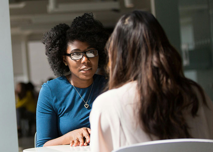 Two women conversing at a table, highlighting potential workplace toxicity signs.