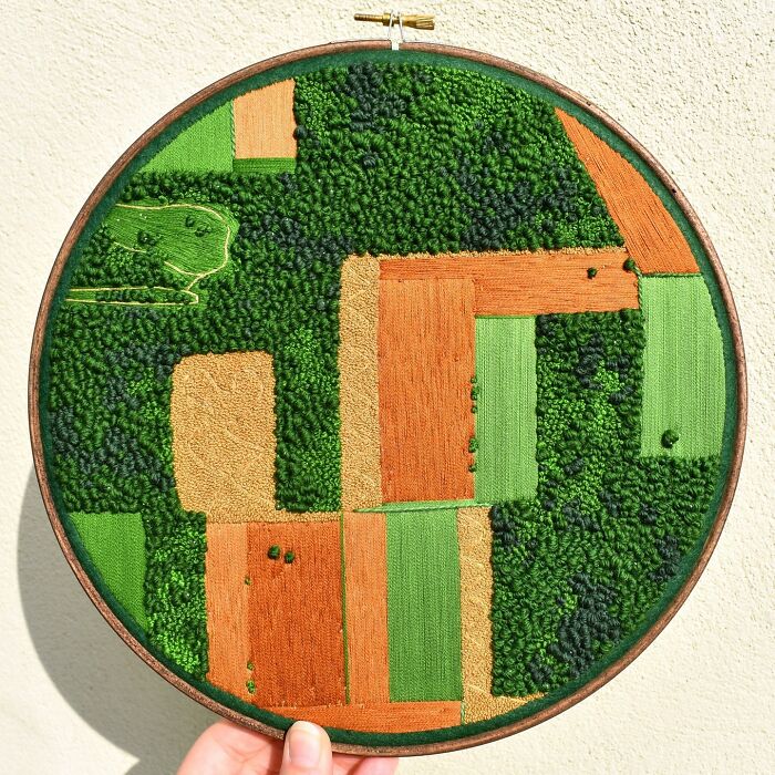 Landscape embroidery art showcasing fields and greenery in a circular frame.