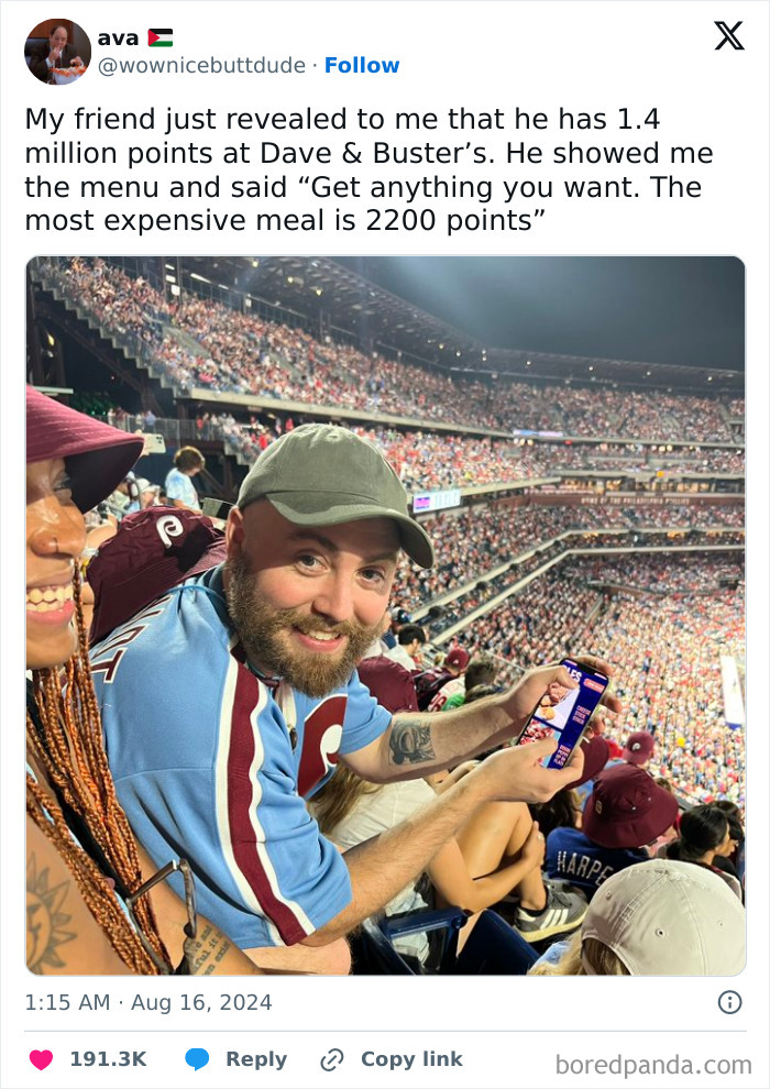 Man smiling at a sports event, holding a phone, illustrating a middle class meme in a crowded stadium.