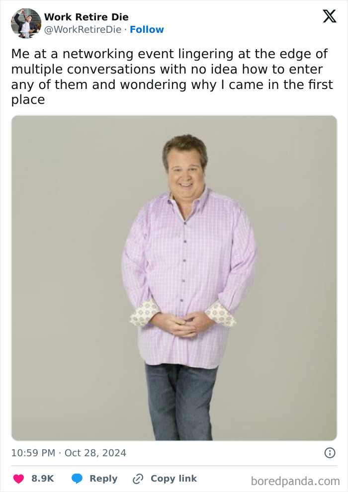 Man in a pink checkered shirt at a networking event, standing awkwardly with hands clasped, capturing work tweet humor.