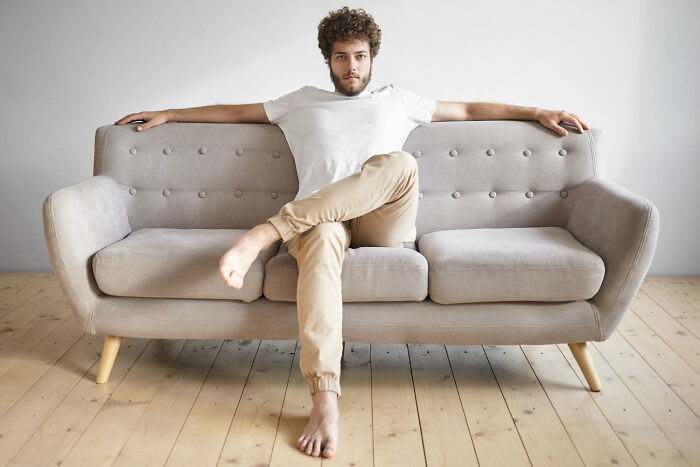 Man sitting barefoot on a neutral-toned couch illustrating poorly-aging interior design trends to avoid in modern homes.