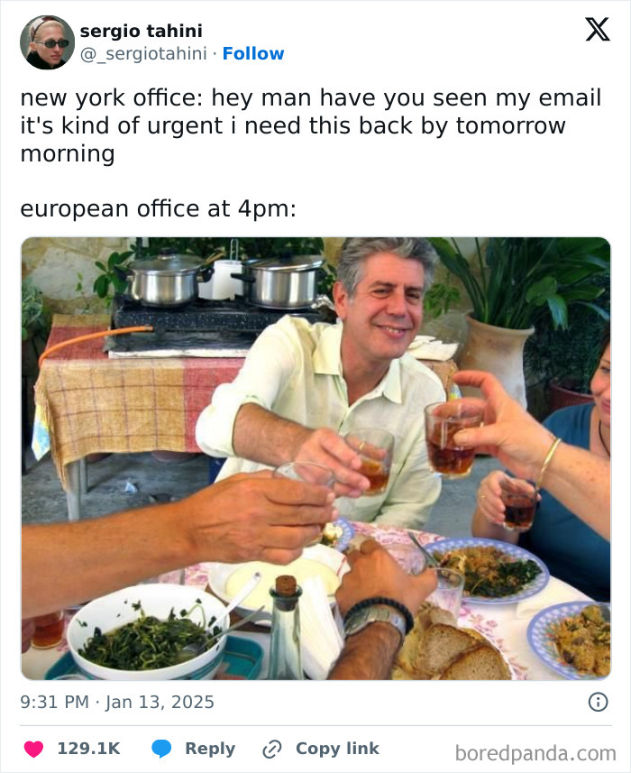 Man at a table raising a glass, smiling, with food and friends around, referencing work tweets humor.