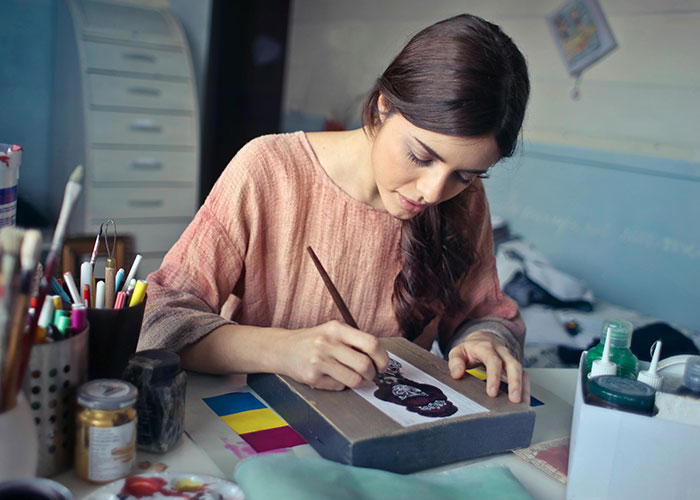 A woman focused on painting in a creative workspace, surrounded by art supplies, illustrating beauty tips in practice.