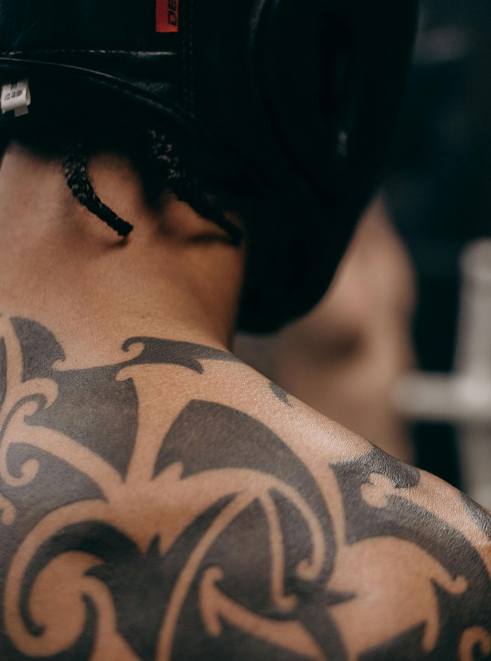 Back view of a person with a large tribal tattoo, wearing a black martial arts headgear.