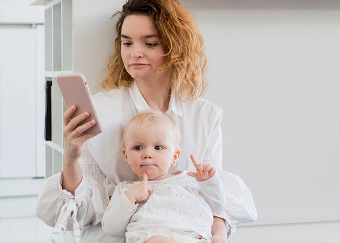 Parent distracted by phone while holding child, illustrating behaviors of a trashy parent.