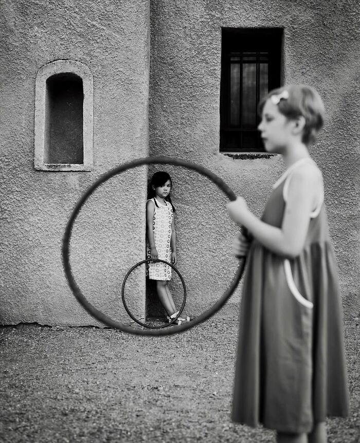 Two children playing with hula hoops, one appearing framed through the hoop, creating a perfectly timed street photo.