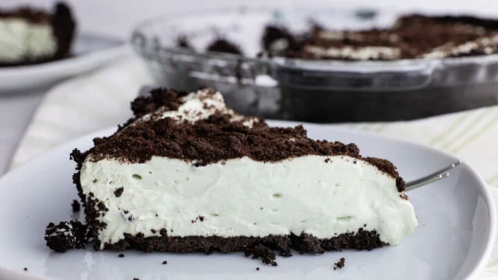 Slice of Watergate Salad pie on a plate with chocolate crust and creamy filling in the foreground.