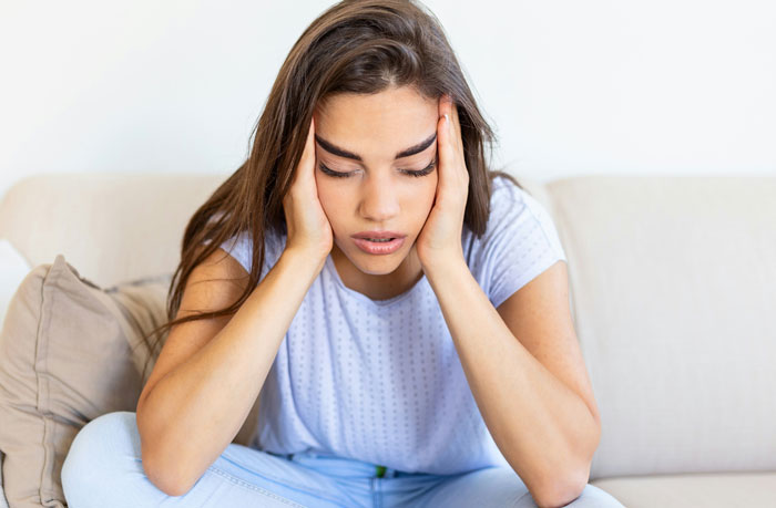 Stressed woman sitting on a couch, holding her head with both hands.