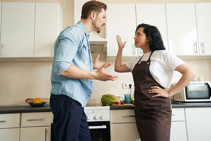 A couple arguing in a kitchen over a promotion, with vegetables on the counter.