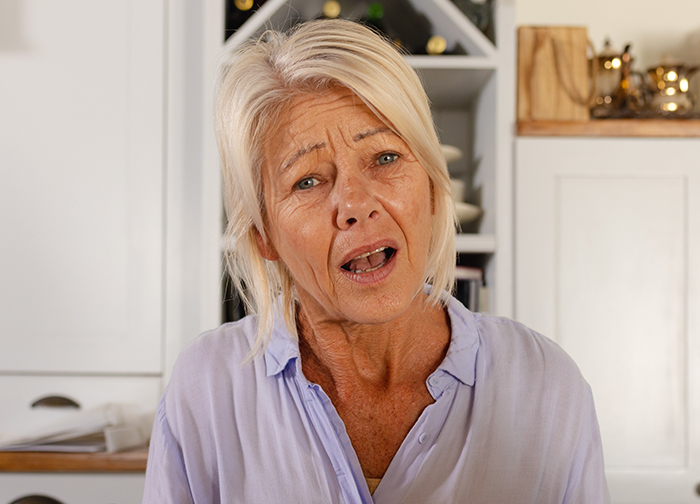 Elderly woman indoors expressing concern, wearing a lavender shirt, related to family dynamics and CPS involvement. Elderly woman indoors expressing concern, wearing a lavender shirt, related to family dynamics and CPS involvement.
