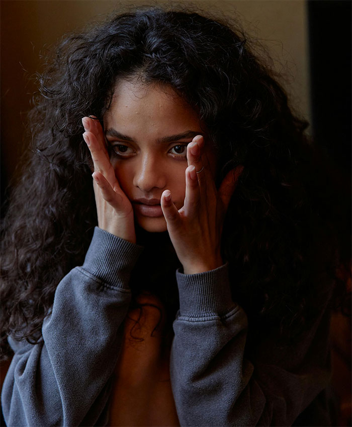 A woman looks distressed after her boyfriend tried to fix her artwork, touching her face with both hands in worry.