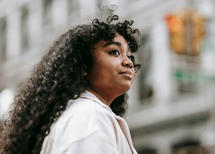 Woman with curly hair on a city street, reflecting beauty tips in urban setting.