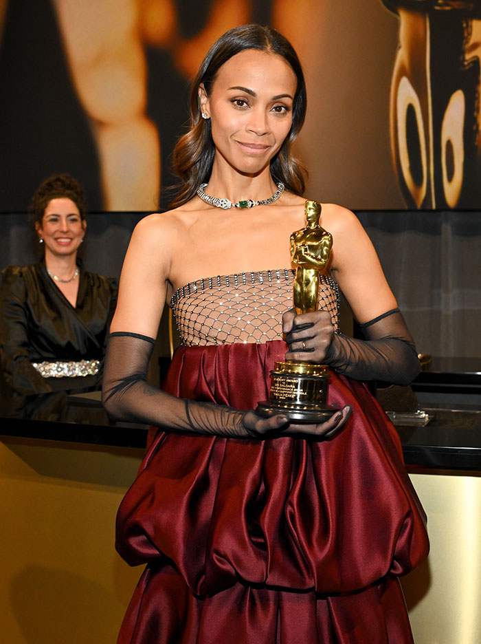 Zoe Salda&ntilde;a holding an Oscar statue, wearing a red and black gown.