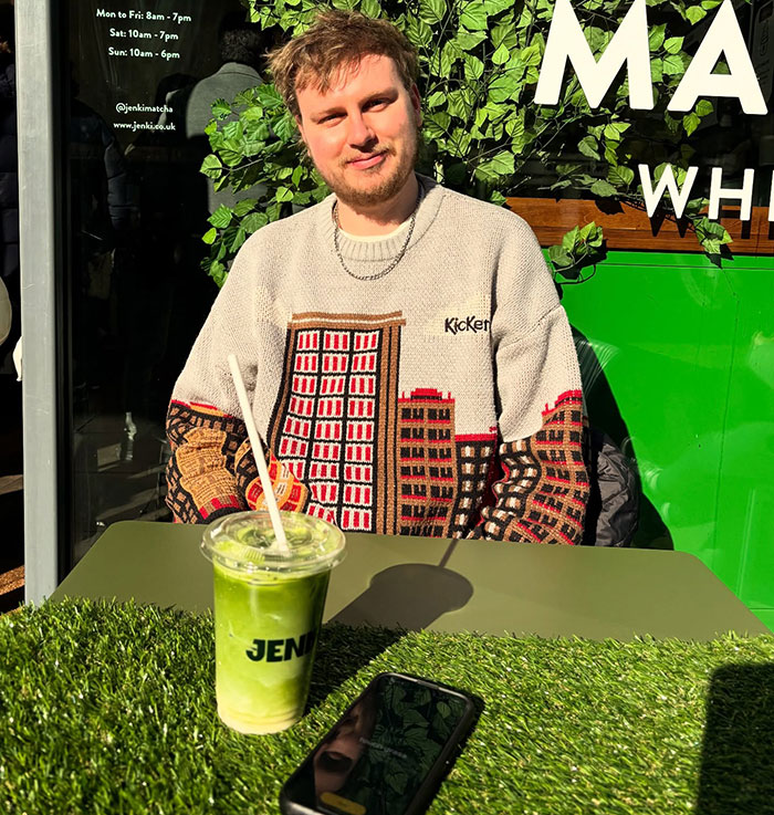 Person sitting at a table with grass covering, next to a smartphone and green drink, related to app controversy.