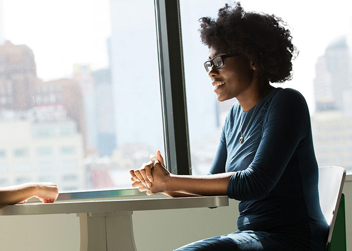 Person smiling and talking in a sunlit room, wearing glasses and a blue shirt, reflecting positive reactions after coming out.