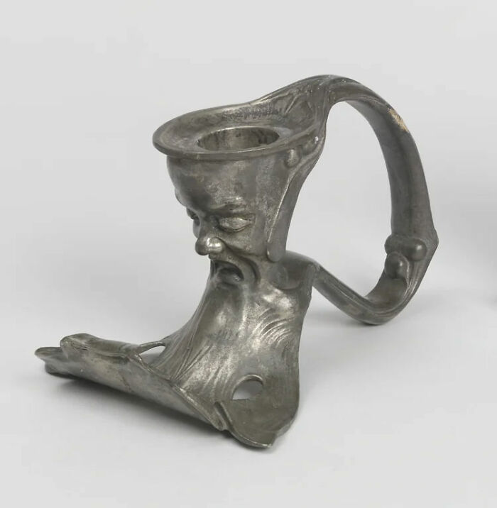 Unsettling antique metal object with a distorted human face and handle.
