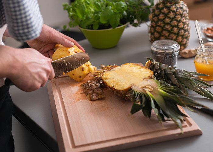 Person slicing pineapple on a wooden board, showcasing food that used to be exotic.