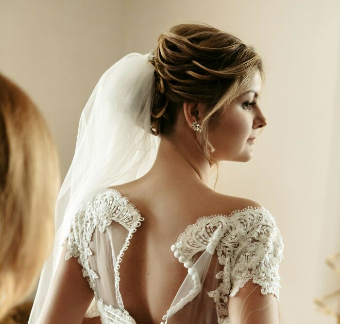 Bride in elegant lace dress and veil, back view, reflecting on wedding day.