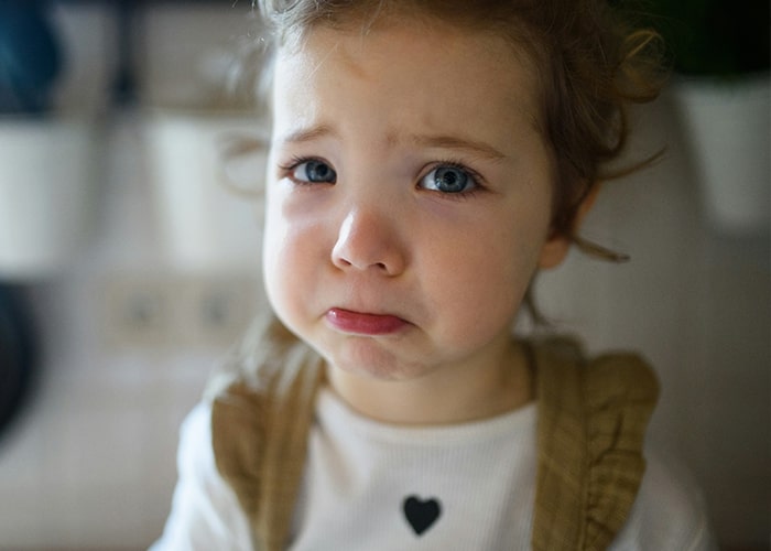 A sad child with curly hair, wearing a white shirt with a heart, illustrating common parenting mistakes.