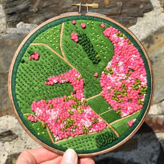 Embroidery landscape art with vibrant pink and green textures, showcasing intricate craftsmanship in a hoop.