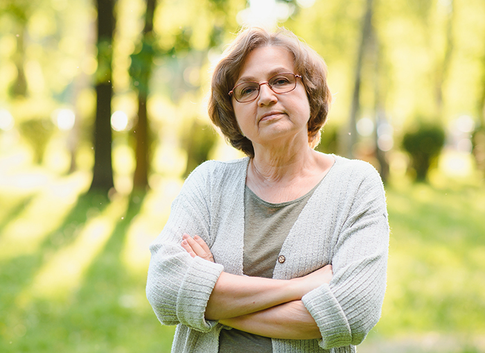 Woman outdoors with crossed arms and glasses, related to OCD and a neighbor's fence issue.