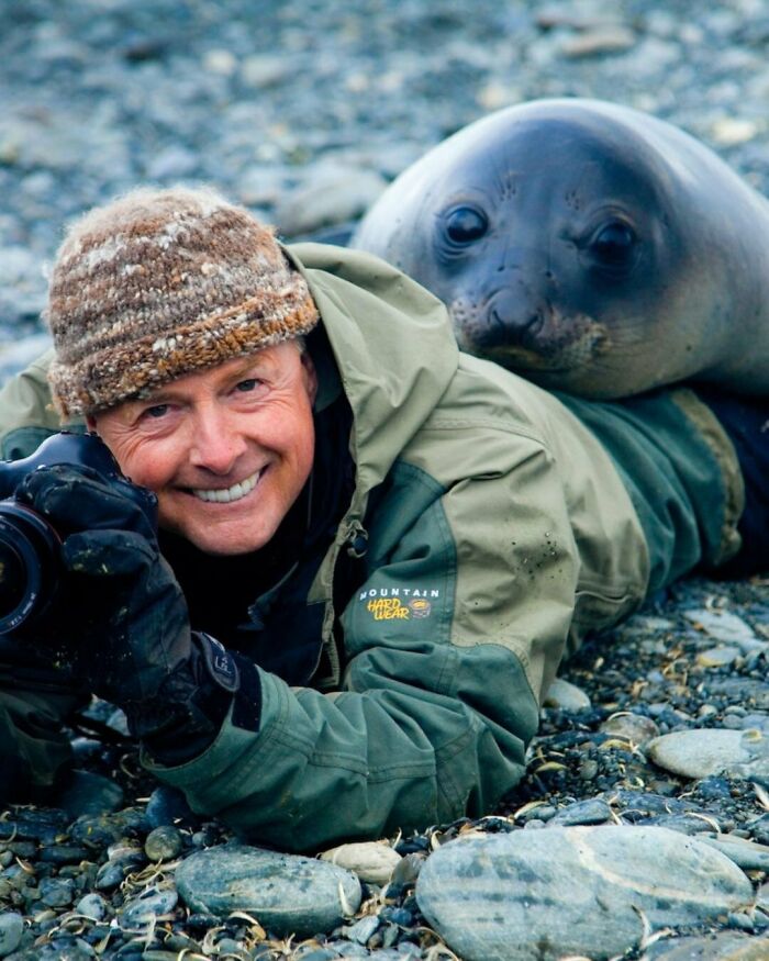 Wildlife photographer smiling as a playful seal rests on his back, showcasing funny animal behavior with no spatial awareness.