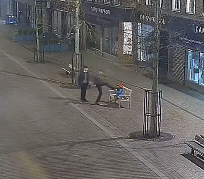 Military personnel damage Paddington Bear statue on a bench at night.