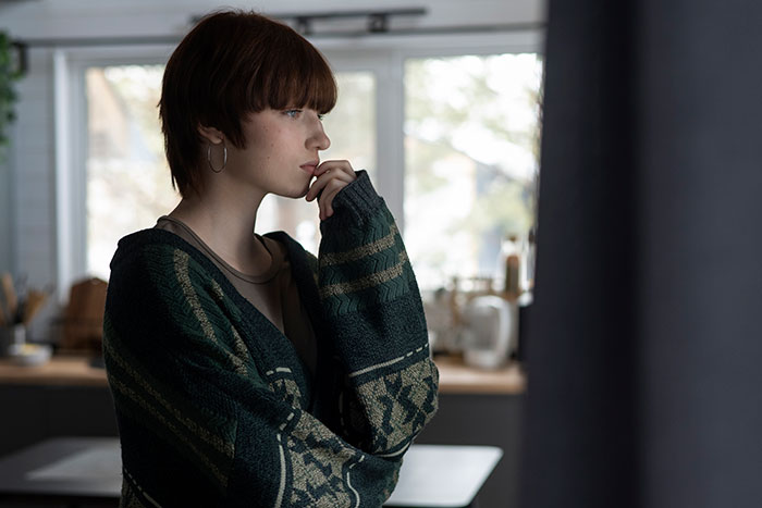 Young woman in a cozy sweater looking thoughtful, standing in a kitchen, pondering about cleansing a friend's home. Young woman in a cozy sweater looking thoughtful, standing in a kitchen, pondering about cleansing a friend's home.