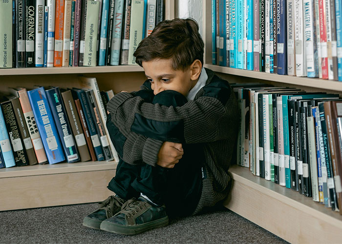 Sad child sitting alone in a library corner, highlighting effects of trashy parenting behaviors.
