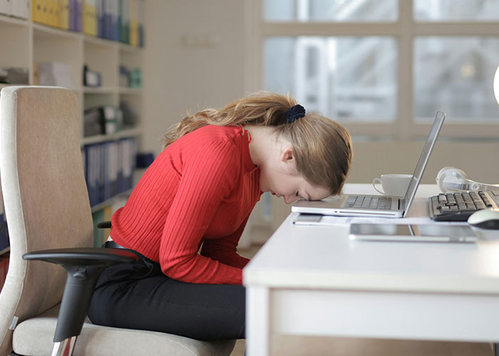 Woman in a red shirt appearing stressed at a desk, illustrating toxic workplace red flags.