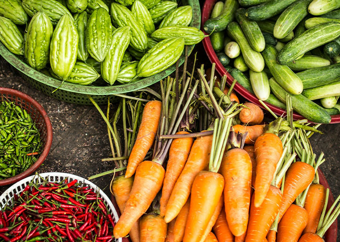 Assorted vegetables including carrots, bitter melons, and cucumbers, once exotic foods, displayed in colorful baskets.