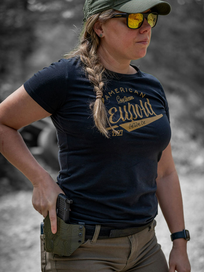 A woman in a cap and sunglasses, holstering a firearm, demonstrating safety tips.