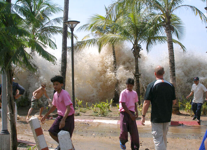 People fleeing a massive wave crashing on a beach, signifying a creepy photo with a dark history.