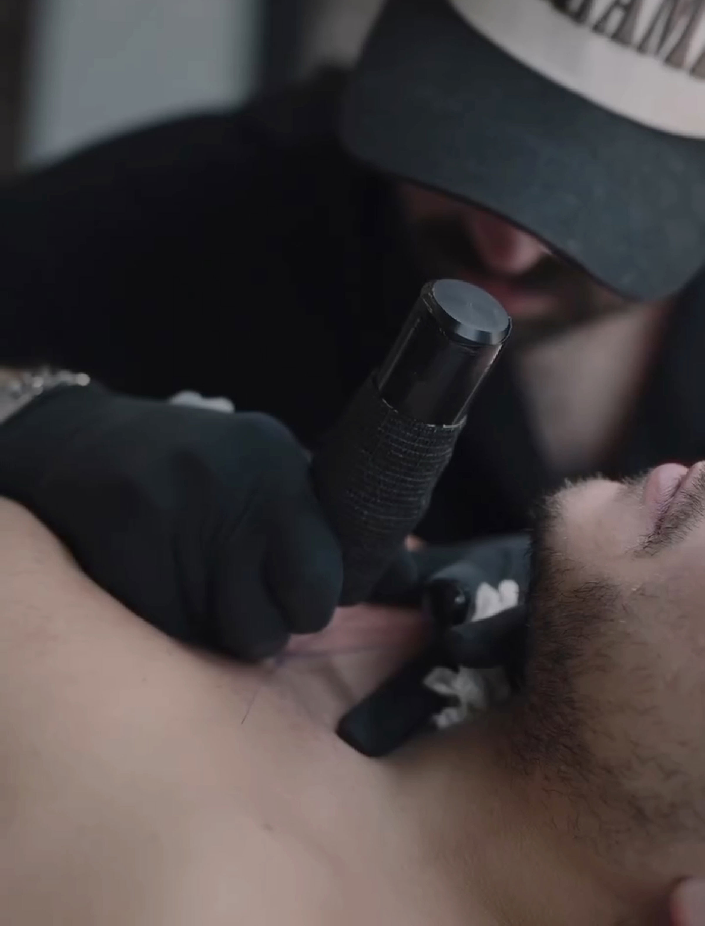Tattoo artist working, wearing a cap, crafts unique brain activity-inspired tattoo on a man's chest.
