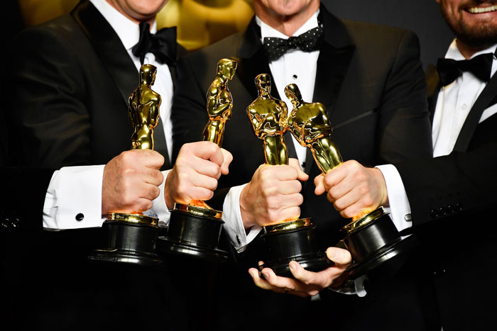 Winners holding Oscars 2025 awards, dressed in tuxedos, celebrating victory.