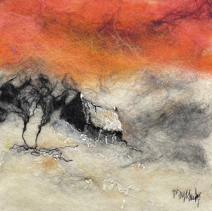 Fiber art depicting a serene landscape with a cottage, trees, and a vibrant orange sky.